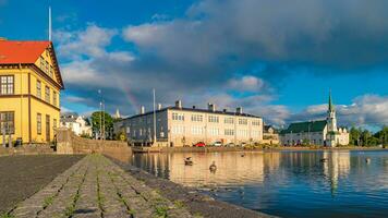 Historical and touristic downtown in Reykjavik at sunset and rainbow in Iceland. Cityscape at golden hour and blue sky at inner lake around Tjornin city park in the downtown. photo