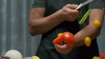 une professionnel chef coupes une tomate tandis que en portant il. proche en haut lent mouvement. video