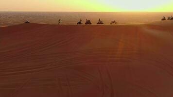 A drone flies over ATVs standing on the sand dunes of the desert against the backdrop of the sunset. Aerial view video