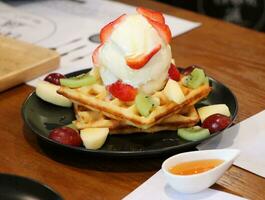 Ice cream on top of wafers and toppings with fruit such as strawberries, kiwi, grapes, and apples photo