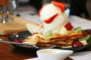 Ice cream on top of wafers and toppings with fruit such as strawberries, kiwi, grapes, and apples photo