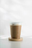 Iced cappuccino in a plastic glass on a white wooden table, minimalist-style picture. photo