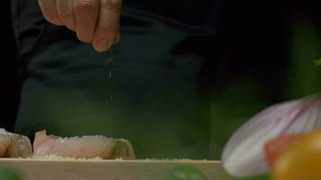 Professional chef sprinkles white fish steak with pepper. Close up slow motion video