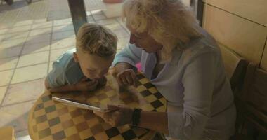 Boy and grandmother entertaining with touch pad in cafe video