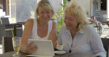 Two senior women watching photos on pad in street cafe video