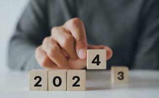 Man hand putting wooden cube block to change 2023 year to 2024 year. start to year 2024. happy new years concept. photo