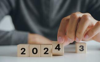 Man hand putting wooden cube block to change 2023 year to 2024 year. start to year 2024. happy new years concept. photo