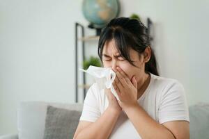 Young woman got a nose allergy sneezing sitting on the sofa at home.  Flu, Influenza, Sick, Fever, Illness. Healthcare and medical concept. photo