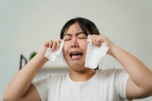 retrato de un triste asiático mujer llorando toallitas su lágrimas con un pañuelo de papel papel toalla. foto