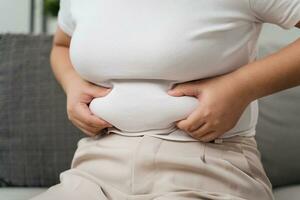 cerca arriba de gordito mujer participación su barriga grasa en el sofá. dieta estilo de vida a reducir barriga y forma arriba saludable, abdominal músculo concepto. foto