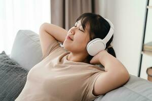 joven mujer escuchando a música con auricular y relajante mientras sentado en el sofá a hogar. foto