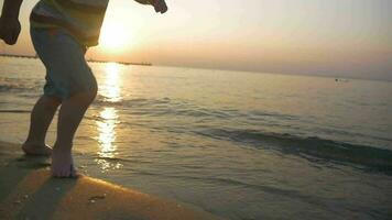 niño corriendo descalzo a lo largo el mar a puesta de sol video