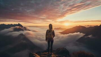 a woman on top of a mountain peak with view of clouds and sunrise photo