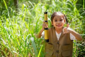 asiático pequeño muchachas explorar naturaleza mediante aumentador lentes y prismáticos en el parque. educación, campo excursiones, investigación, y descubrimiento conceptos. foto