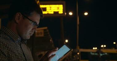 Man with tablet computer on bus station at night video