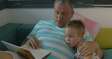 niño y abuelo utilizando ordenador portátil a hogar video