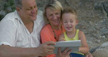 moeder vader en zoon aan het kijken video Aan stootkussen terwijl zittend Aan strand