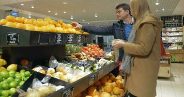 feliz casal escolhendo laranjas dentro supermercado video