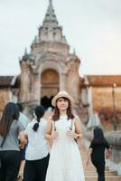 Young asian woman traveler in white dress with hat and bag traveling in Wat Phra That Lampang Luang, Tourist visit at Lampang, Thailand.. Asia Travel, Vacation and summer holiday concept photo