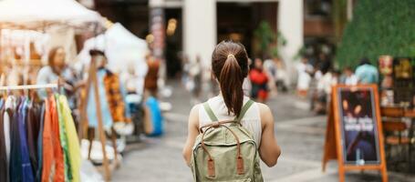 Young asian woman traveler in Yellow dress with bag traveling to NIMMAN on Nimmanhaemin Road, Tourist visit at the Night market city in Chang Mai, Thailand. Asia Travel, Vacation and summer holiday photo