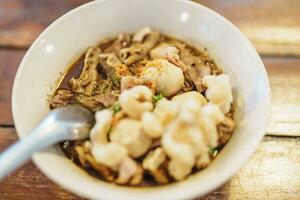 Thai Boat noodle thicken soup with Pork, balls, crispy fried pork skin, basil leaf and Vegetables. Traditional and Famous Street food in Thailand photo