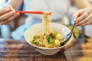 Woman eating Thai Boat noodle thicken soup with Pork, balls, crispy fried pork skin, basil leaf and Vegetables. Traditional and Famous Street food in Thailand photo