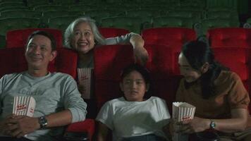 Aziatisch familie publiek genieten aan het kijken bioscoop samen Bij film theaters. kind en ouders hebben binnen- vermaak levensstijl met prestatie film kunst show, gelukkig en vrolijk met popcorn en glimlach. video