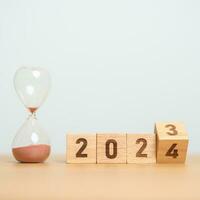 flipping block 2023 to 2024 text with hourglass on table. Resolution, time, plan, goal, motivation, reboot, countdown  and New Year holiday concepts photo