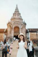 Young asian woman traveler in white dress with hat and bag traveling in Wat Phra That Lampang Luang, Tourist visit at Lampang, Thailand.. Asia Travel, Vacation and summer holiday concept photo