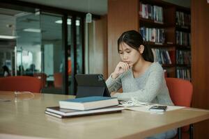 asiático estudiante mujer leer libros en biblioteca a universidad. joven niña estrés cansado tener problema mientras estudiar duro. tristeza concepto foto