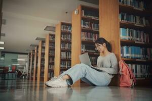 Student girl sitting on floor and using laptop, Writes notes for paper, Essay, Study for class assignment. Diverse group of Students Learning, Studying for Exams. photo