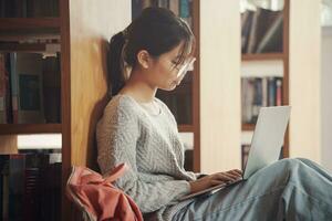 Student girl sitting on floor and using laptop, Writes notes for paper, Essay, Study for class assignment. Diverse group of Students Learning, Studying for Exams. photo