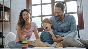 felicidad hijo jugando juguete con madre y padre en cama, disfrutar relajante juntos a hogar. foto