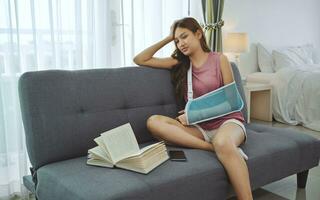 Unhappy young woman wearing soft splint due to sore arm sitting on sofa at home. photo