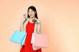 Young woman carrying shopping bags with using credit card and mobile phone standing over isolated on pink background. photo