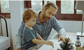 Caucasian family painting on paper with son indoors in house. Little son learn how to draw art picture enjoy creativity with father in house. photo