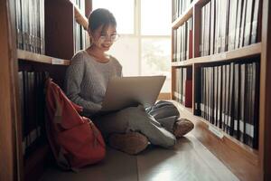 Student girl sitting on floor and using laptop, Writes notes for paper, Essay, Study for class assignment. Diverse group of Students Learning, Studying for Exams. photo