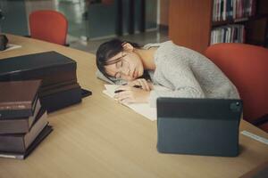 cansado estudiante niña con lentes acostado en libros en biblioteca. foto
