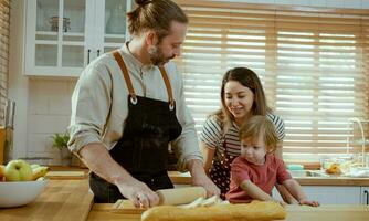 Happy young family enjoying making pie dough or pastries in modern kitchen together, very happy parents teaching little son how to cook bakery at home. photo