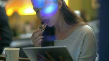 brunetta donna mangia torta mentre lettura su elettronico tavoletta video