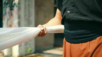 an Asian man pulls a white cloth tied to an old building by his hand video