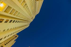 Vertical shot from bottom to top of illuminated skyscraper against blue sky photo