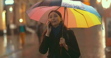 morena mulher fala em a telefone em a rua em chuvoso dia video