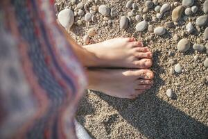 close-up photo of a girl's legs in a skirt in pebbles and sand on the beach