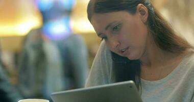 Woman busy with phone talk and using pad in cafe video