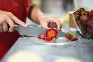 pastry chef cuts strawberries with a knife for baking sweet desserts photo