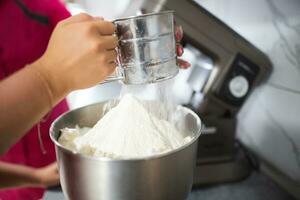 the cook sifts flour through a sieve to knead the dough photo