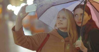 dos mujer amigos haciendo selfie con paraguas en lluvioso día video