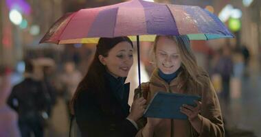 fêmea amigos usando toque almofada em chuvoso tarde dentro cidade video