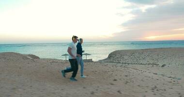 joven personas trotar en el playa a puesta de sol video